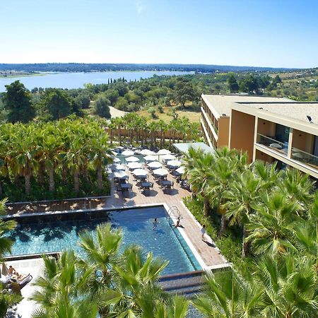 Ap Lago Montargil - Conference & Spa Екстериор снимка The photo shows a scenic view of a modern hotel or resort. In the foreground, there is a swimming pool surrounded by palm trees, with lounge chairs positioned beside it. Sun umbrellas provide shade over the chairs. The background features a lush land