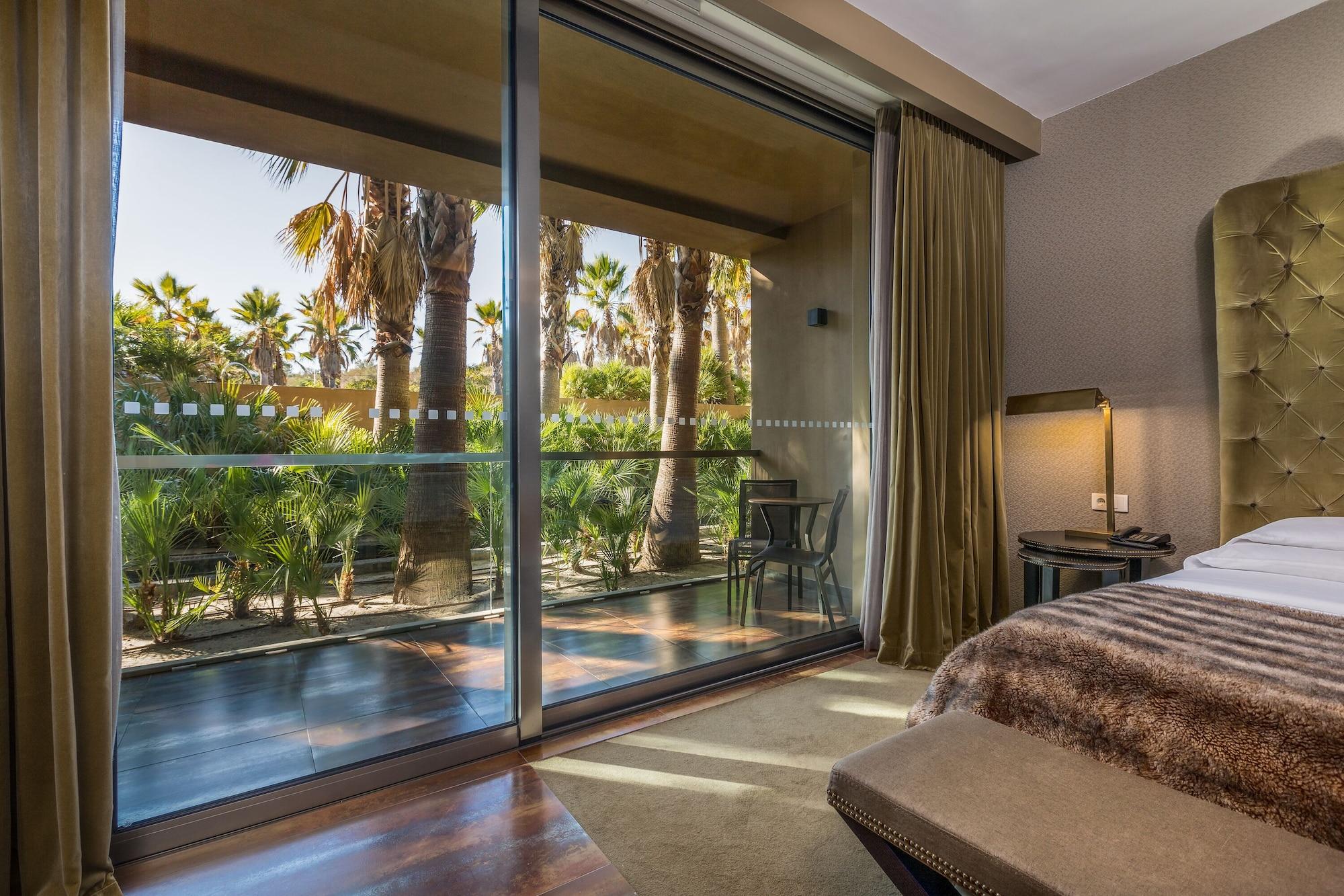 Ap Lago Montargil - Conference & Spa Екстериор снимка The photo shows a bedroom with large glass doors that lead out to a balcony or terrace. The view outside features palm trees and lush greenery, indicating a tropical or warm climate. Inside the room, there is a bed, a bedside table with a lamp, and a