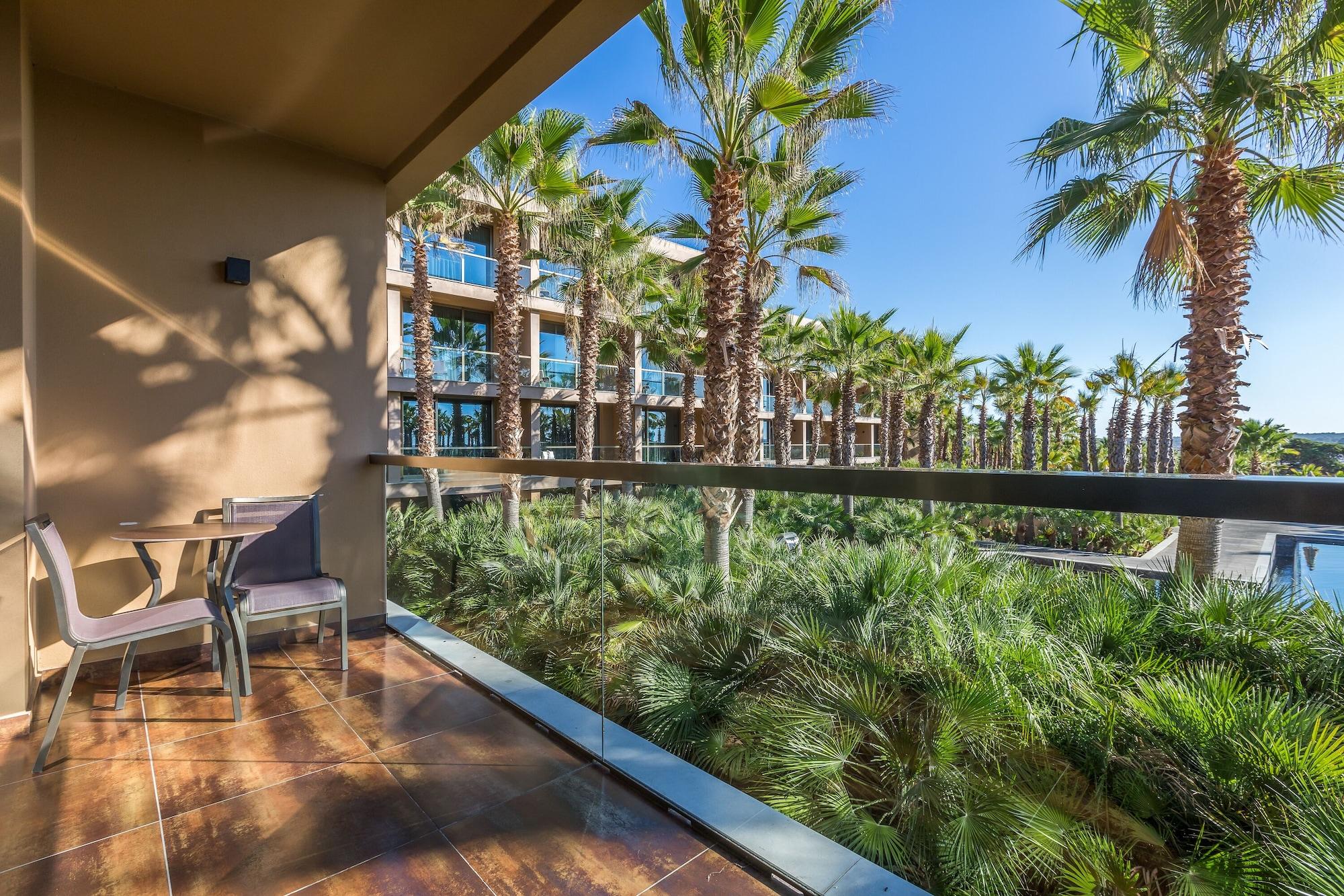 Ap Lago Montargil - Conference & Spa Екстериор снимка The photo shows a balcony with modern furniture, including a chair and a small table. In the background, there are tall palm trees and lush greenery, suggesting a tropical or resort-like setting. The buildings in the distance are likely part of a hot
