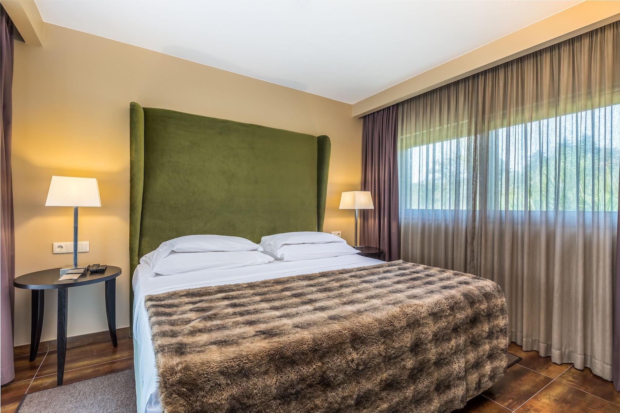 Ap Lago Montargil - Conference & Spa Екстериор снимка The photo shows a cozy hotel room featuring a large bed with two white pillows and a fur-style blanket draped over it. Behind the bed is a tall, green headboard that adds a touch of color to the room. On either side of the bed are bedside tables, eac