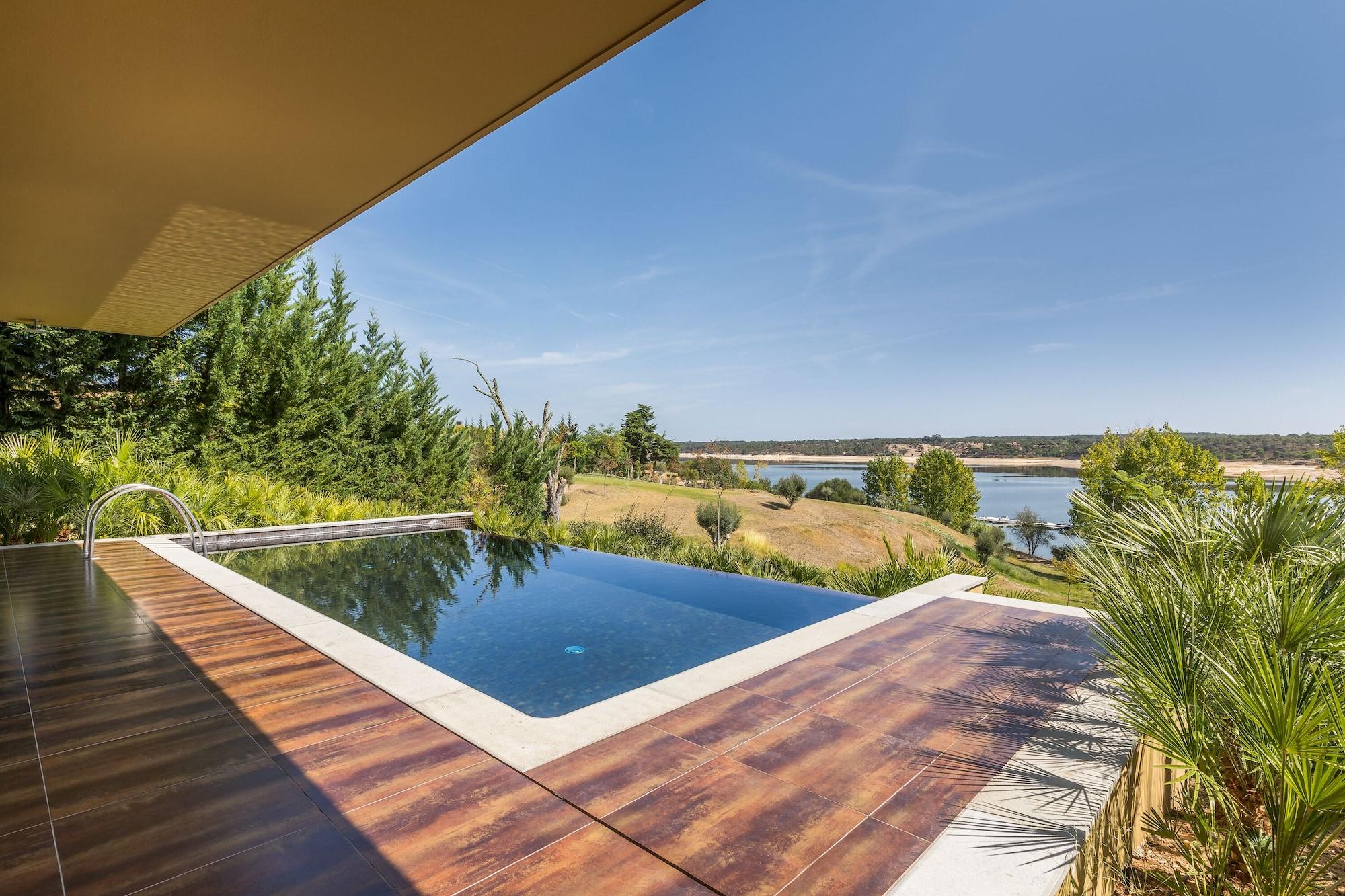 Ap Lago Montargil - Conference & Spa Екстериор снимка The photo shows a luxurious infinity pool situated on a terrace or deck. The pool features a sleek, modern design with a dark blue surface that reflects the surrounding scenery. In the background, there is a landscape of rolling hills and a body of w