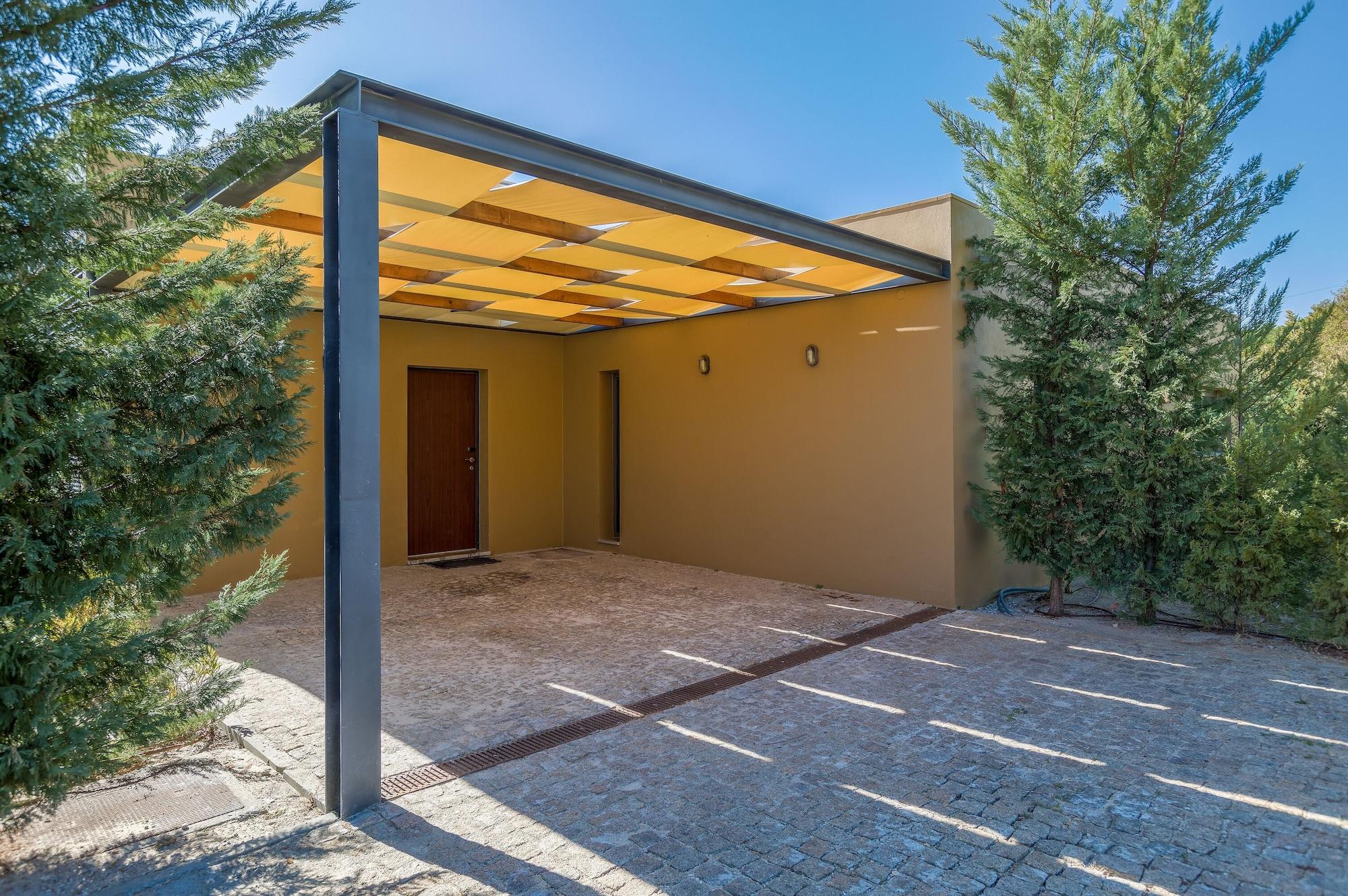 Ap Lago Montargil - Conference & Spa Екстериор снимка The photo shows an exterior view of a modern structure with a carport. The carport has a sleek, metallic frame and a yellowish canopy above it. In front of the structure, there is a paved area made of stone or tiles. The main entrance features a wood