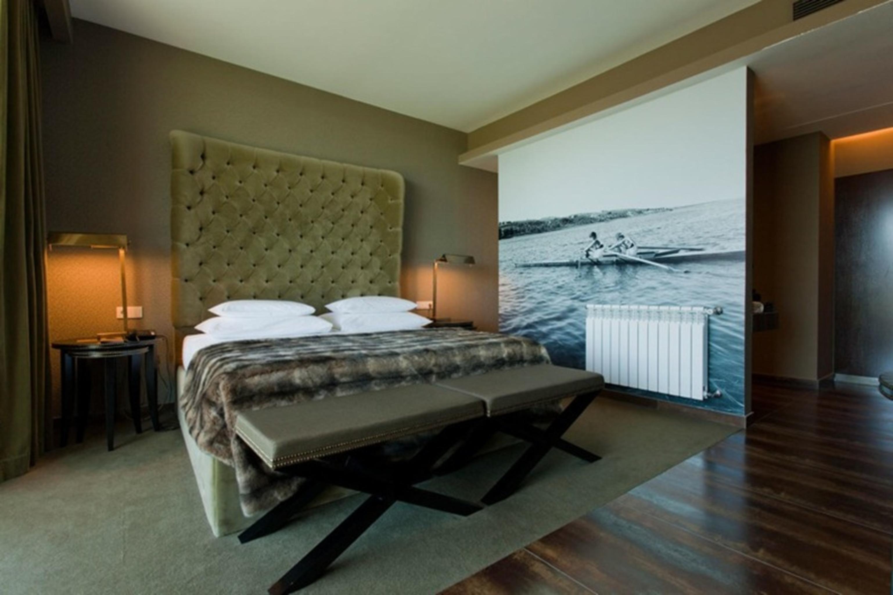 Ap Lago Montargil - Conference & Spa Екстериор снимка The photo shows a modern hotel room featuring a large bed with a tufted headboard and plush bedding. The color palette is neutral, with shades of green and gray. On one side of the room, there are bedside tables with lamps. A comfortable bench sits a
