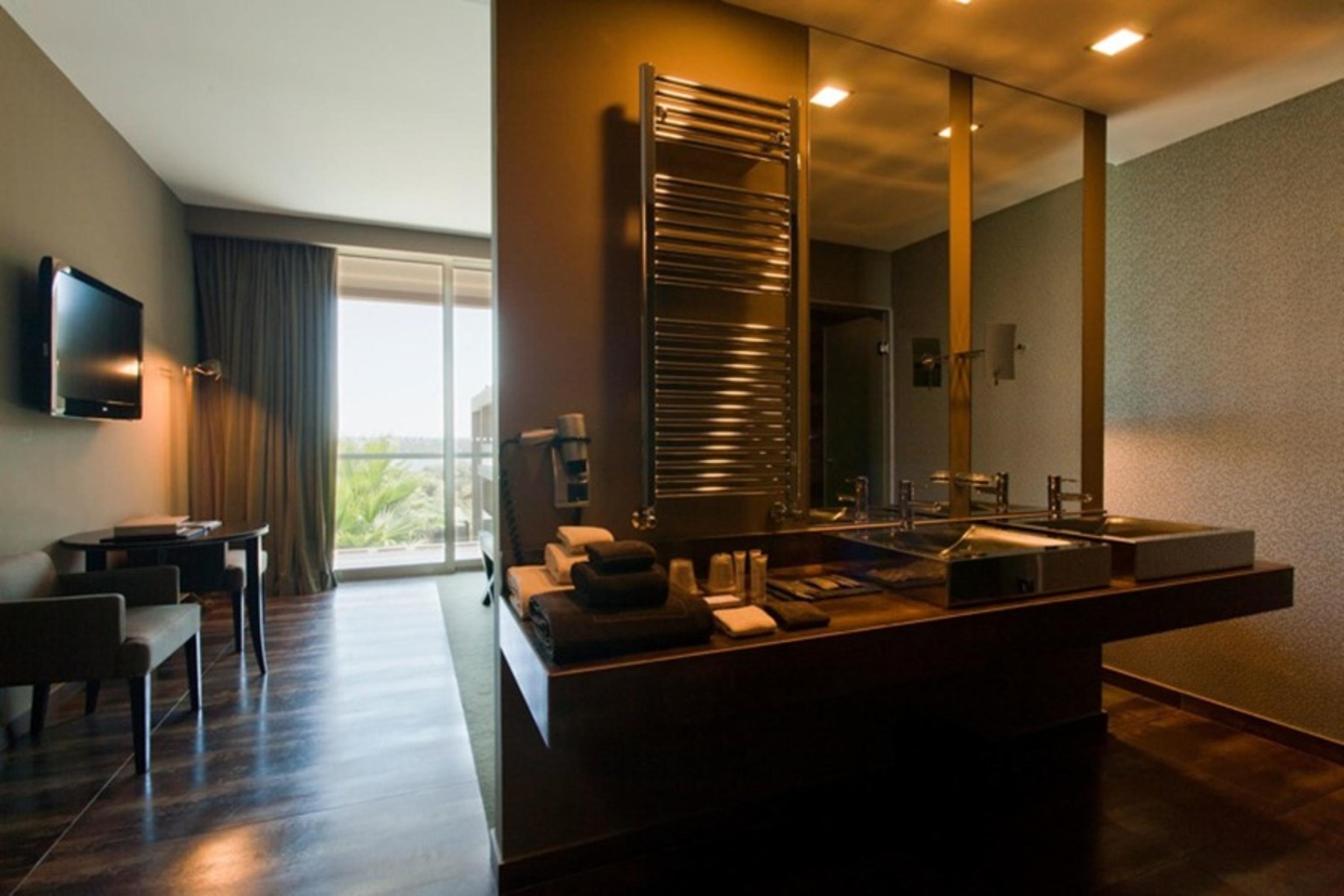 Ap Lago Montargil - Conference & Spa Екстериор снимка The photo displays a modern hotel room with a contemporary design. The room features a large window, allowing natural light to enter and offering a view outside. On one side, there is a sitting area with a small table and chairs. The other side showc