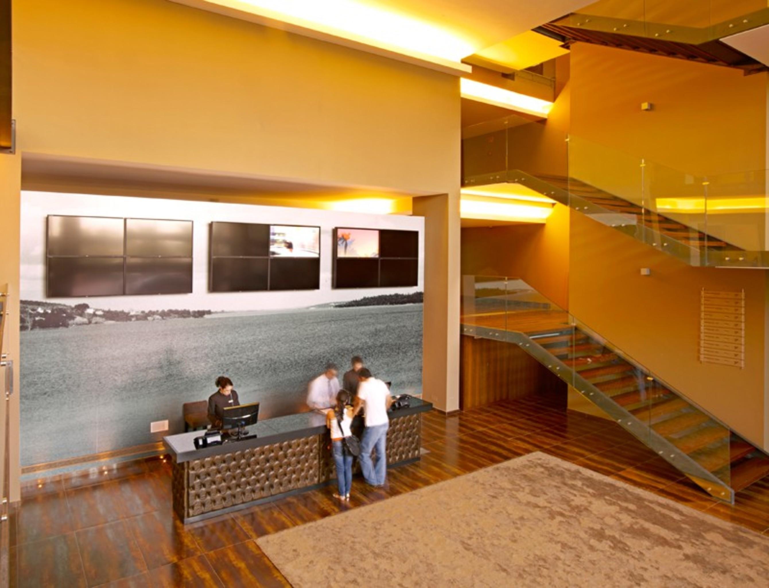 Ap Lago Montargil - Conference & Spa Екстериор снимка The photo depicts a modern lobby area with a reception desk. The design features a combination of warm colors and wood flooring. In the background, there is a large wall-mounted screen or display, showcasing several monitors. The wall behind the desk