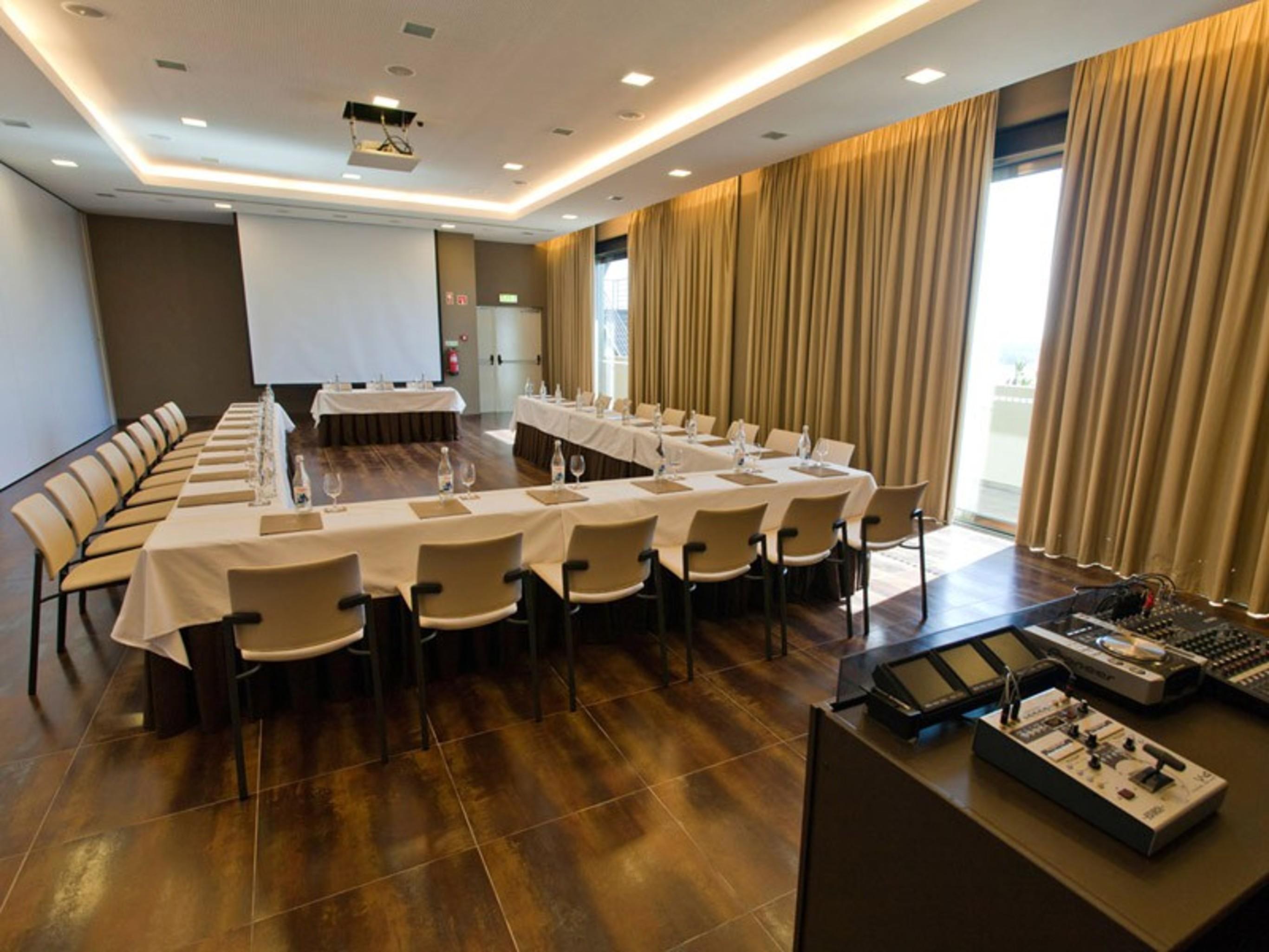 Ap Lago Montargil - Conference & Spa Екстериор снимка The photo shows a modern conference room set up for a meeting. There are several tables arranged in a U-shape, surrounded by chairs. A large screen and projector are positioned at the front, with a table for speakers or presenters. The room has large