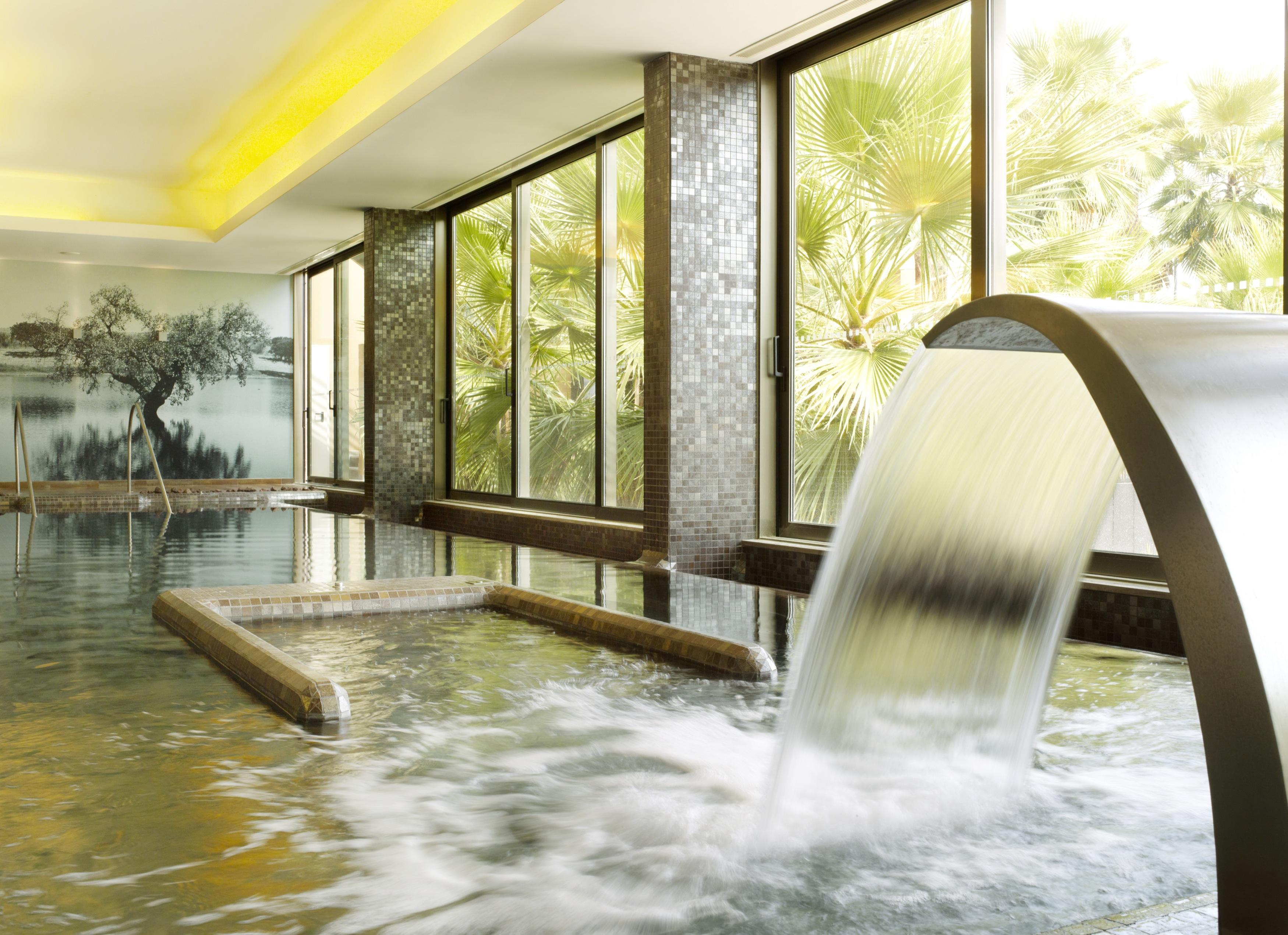 Ap Lago Montargil - Conference & Spa Екстериор снимка The photo depicts a serene spa environment featuring a tranquil indoor pool area. There is a sleek, modern water feature that spills water gracefully into the pool. Large windows allow natural light to flood the space, showcasing views of lush greene