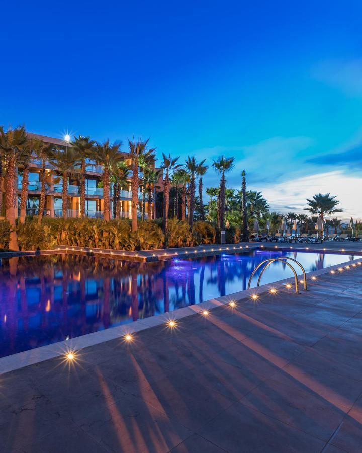 Ap Lago Montargil - Conference & Spa Екстериор снимка The image shows a serene and inviting outdoor area with a large swimming pool that features a beautiful blue hue, likely illuminated by lights. Surrounding the pool are well-maintained palm trees and lush greenery, creating a tropical atmosphere. In 
